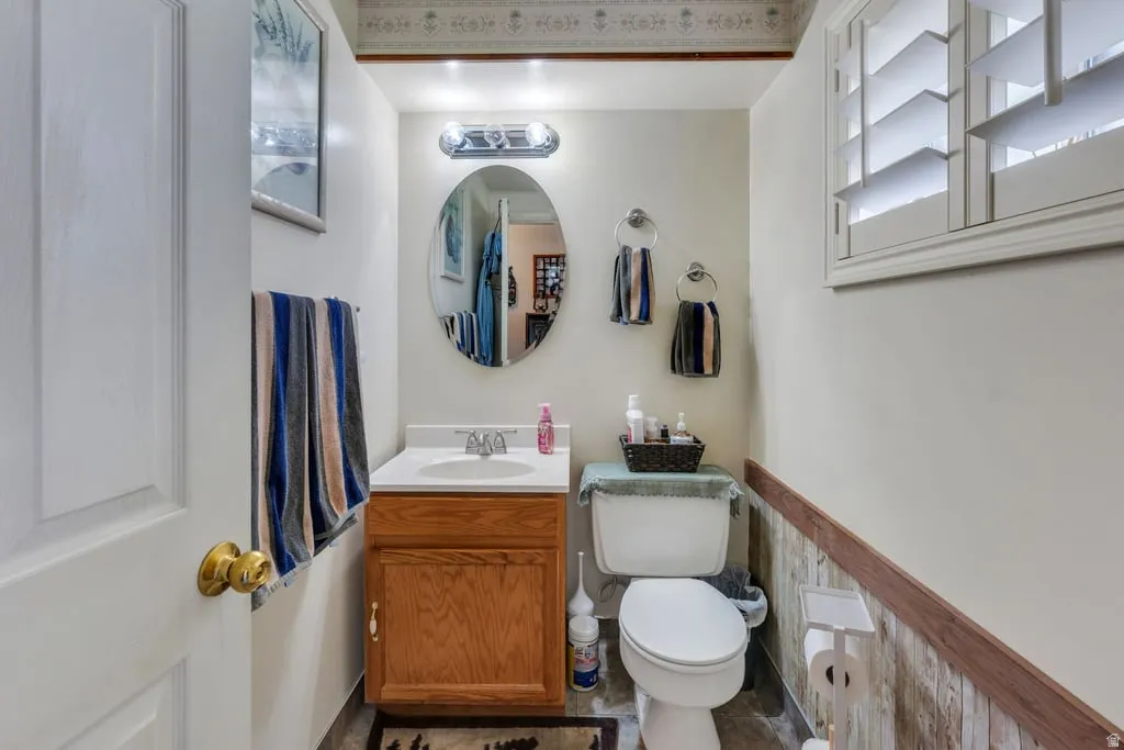 Powder room featuring a wood-finish vanity with an integrated sink, an oval mirror, and a window with white plantation shutters