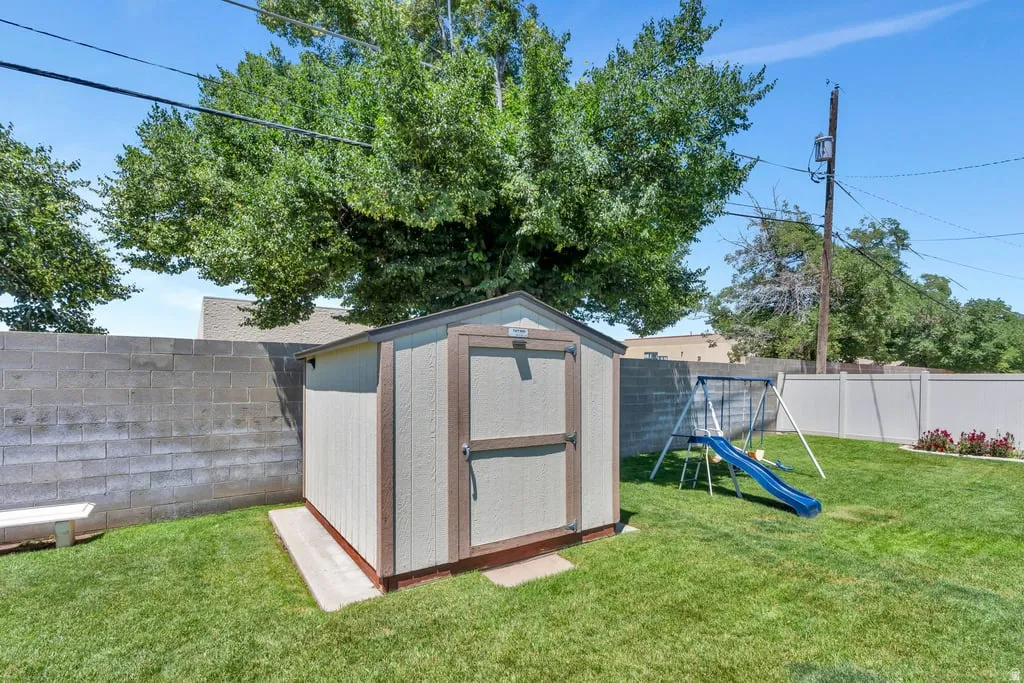Backyard featuring a wooden storage shed on a concrete pad, a manicured lawn, and mature trees