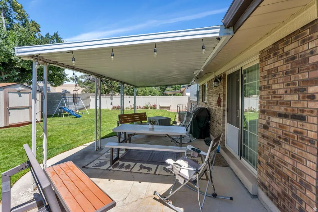 Expansive backyard featuring a covered patio with integrated lighting, a manicured lawn, a storage shed, and brick exterior siding