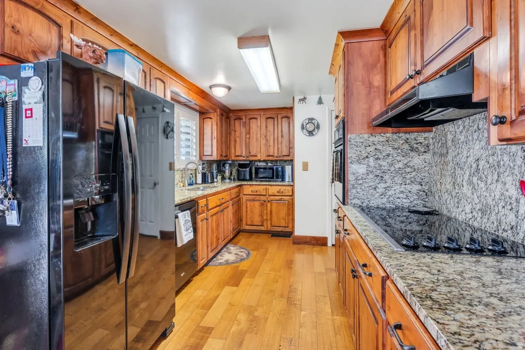 Kitchen featuring rich wood cabinetry, granite countertops, integrated cooktop, wall oven, and wood-finish flooring