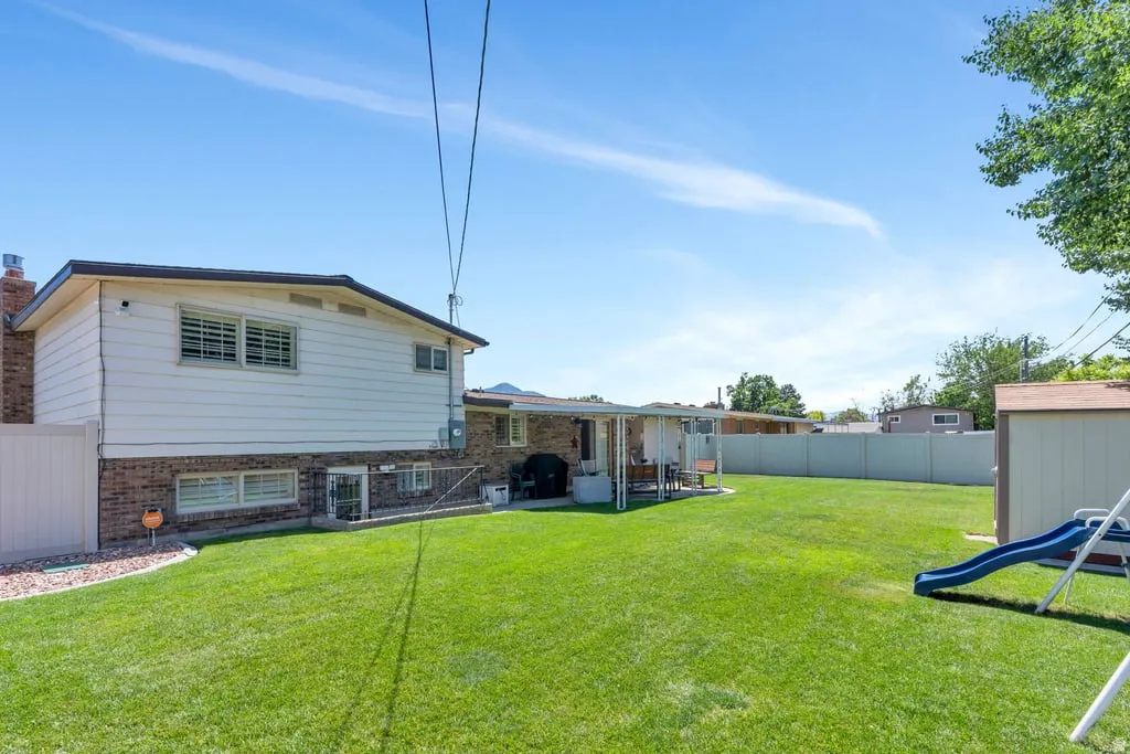 Expansive backyard featuring a manicured lawn, a covered patio area, and a storage shed