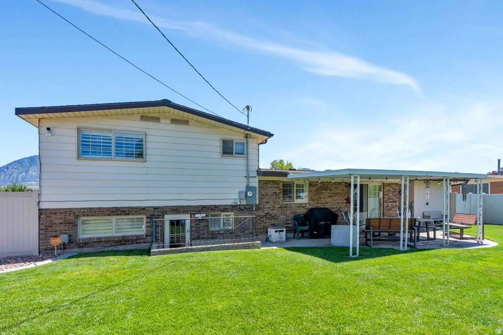 Expansive backyard featuring a manicured lawn, a covered patio, brick and siding exterior, and a mountain backdrop