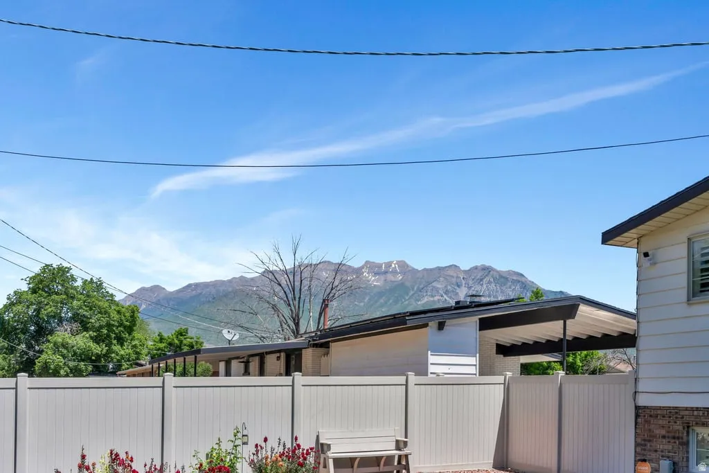 Property exterior featuring a white privacy fence, a mountain backdrop, mature trees