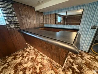Built-in bar with dark countertop and wood-paneling base