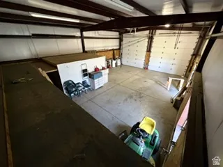 Spacious garage featuring concrete flooring, multiple overhead doors, exposed structural beams, and integrated overhead lighting
