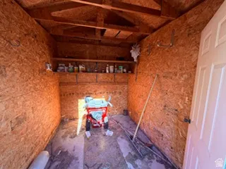 Storage shed featuring OSB paneling, exposed rafters, built-in shelving, wall-mounted hooks, and a paneled door
