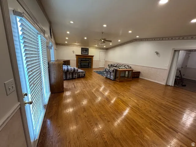 Living room with a glass covered fireplace, hardwood floors, recessed lighting, and a ceiling fan