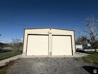 Metal-sided outbuilding featuring two large roll-up doors, a concrete pad, and a gravel approach