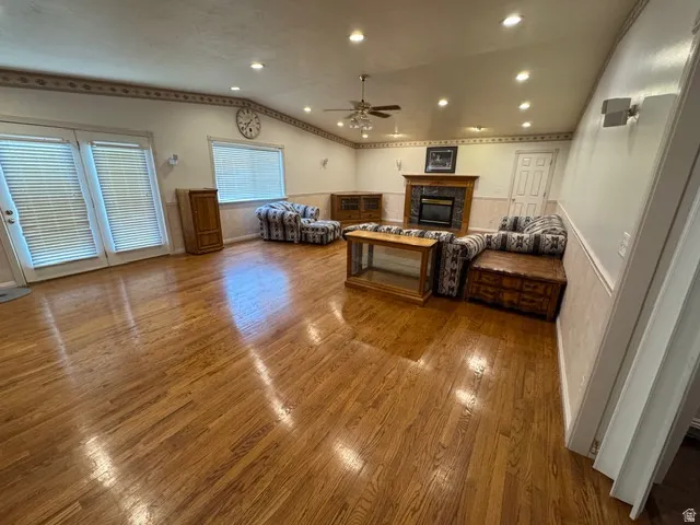 Great room featuring hardwood flooring, a glass covered fireplace, ceiling fan, recessed lighting, and vaulted ceiling