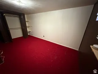 Room with red carpet flooring, light-toned walls, and a built-in closet with dark wood-finish bi-fold doors