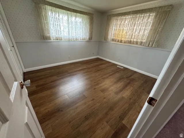 Unfurnished bedroom featuring dark wood-style laminate flooring, wallpapered walls, and a closet