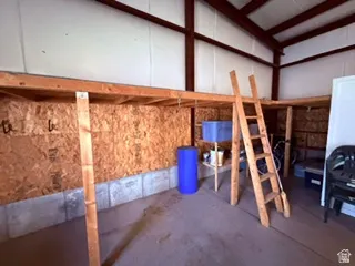 Interior space featuring a concrete floor, built-in wooden mezzanine storage, exposed metal beams, and insulated panel walls