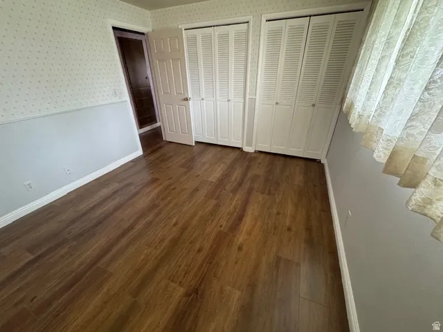 Unfurnished bedroom featuring two closets, dark wood-style laminate flooring, and wallpapered walls