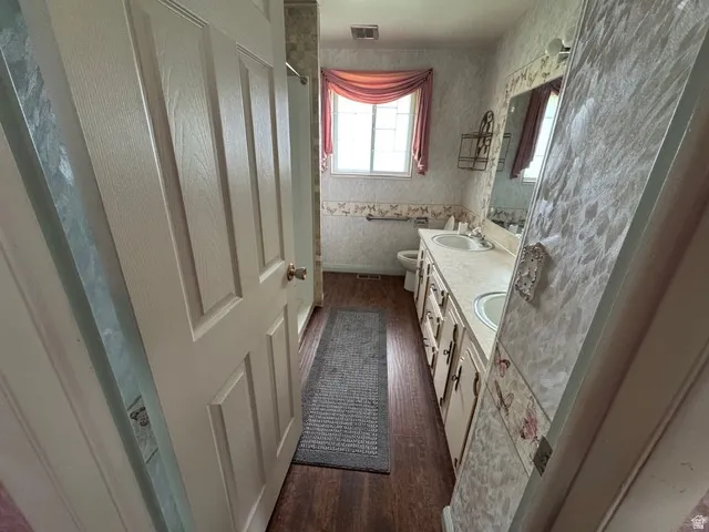 Bathroom with double vanity, curtained shower, and dark wood-style laminate flooring