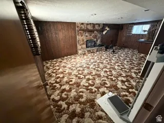 Spacious room featuring a stone-clad fireplace and hearth, wood paneling, patterned carpet, and a window with blinds