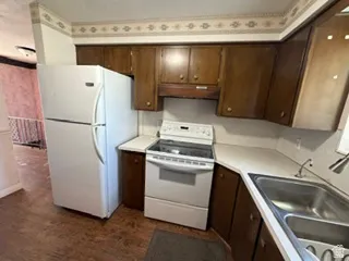 Kitchen featuring wood-finish cabinetry, a double basin stainless steel sink, and white countertops