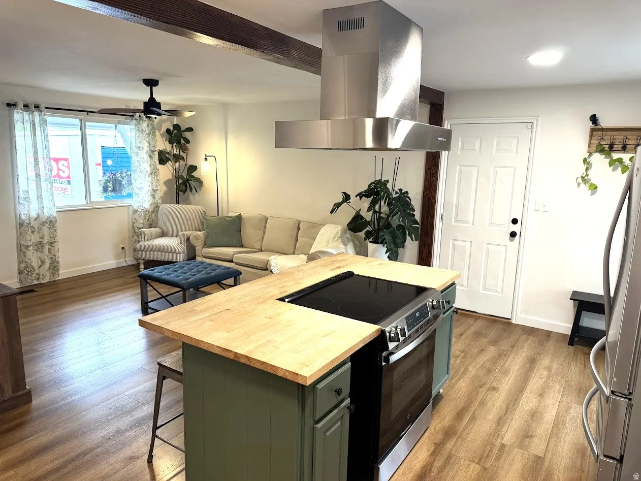 Open-concept living space featuring wood-finish flooring, a kitchen island with a wood countertop, and a stainless steel range hood