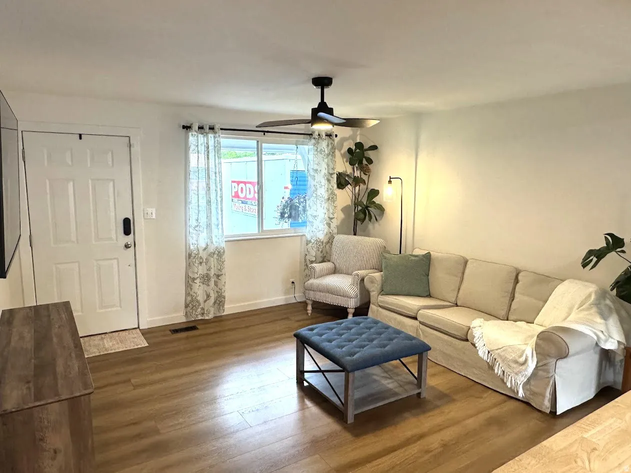 Living area featuring wood-finish flooring, a white paneled entry door, and a ceiling fan