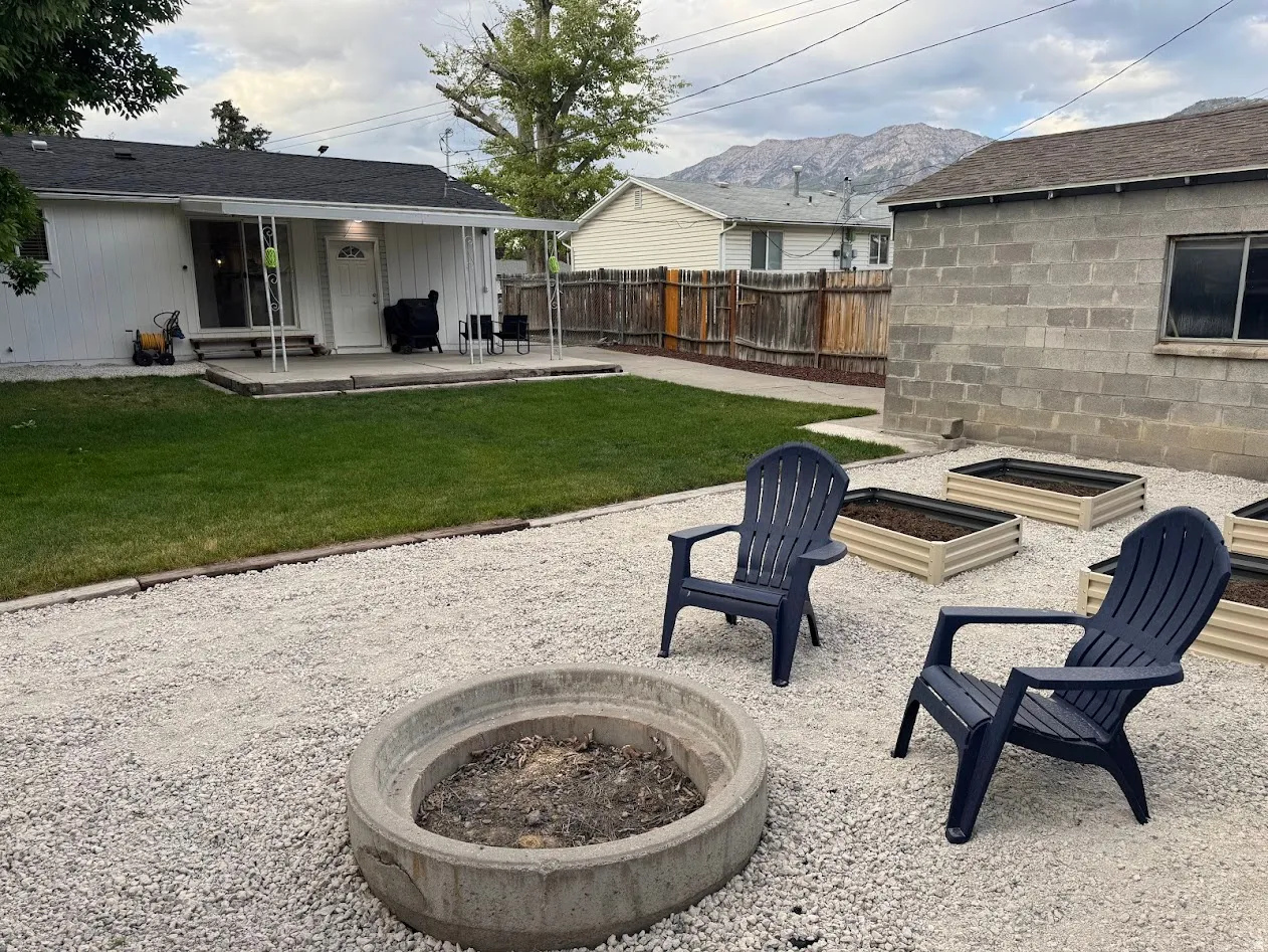 Expansive outdoor space featuring a fire pit area with gravel ground cover, an adjacent grassy lawn, and raised garden beds