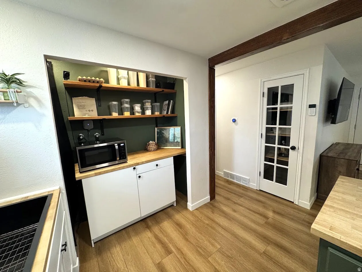 Dedicated pantry area featuring open wood shelving, a butcher block countertop, and white base cabinetry