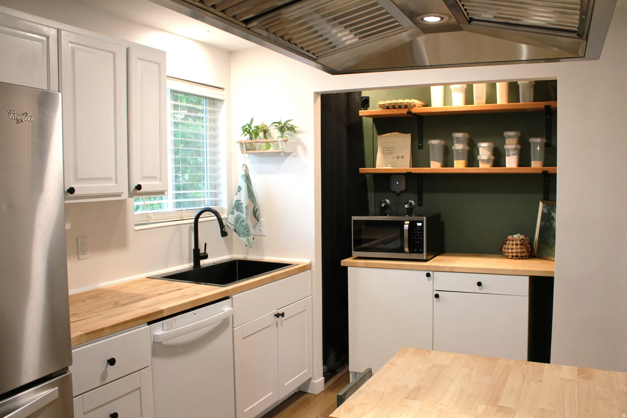 Modern kitchen featuring light wood-finish countertops, white cabinetry with black hardware, a stainless steel refrigerator, and a black basin sink with a matching faucet