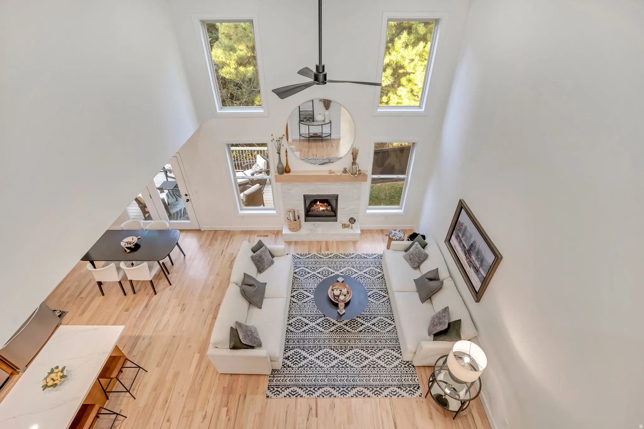 Soaring ceilings featuring a modern ceiling fan, a white brick fireplace with a wood mantle, and multiple windows