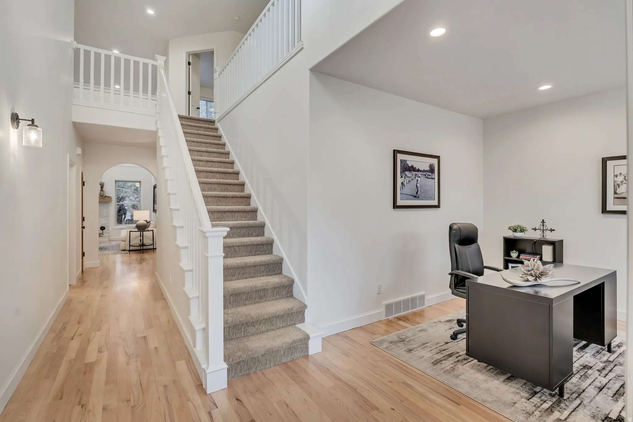 Inviting entryway featuring wood-finish flooring, a carpeted staircase with white railings, and a dedicated office space with recessed lighting