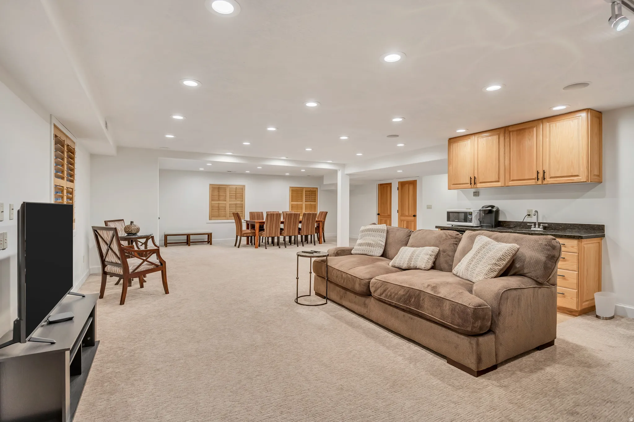 Carpeted recreation area featuring recessed lighting, a wet bar with wood cabinetry and dark countertops, and interior window shutters