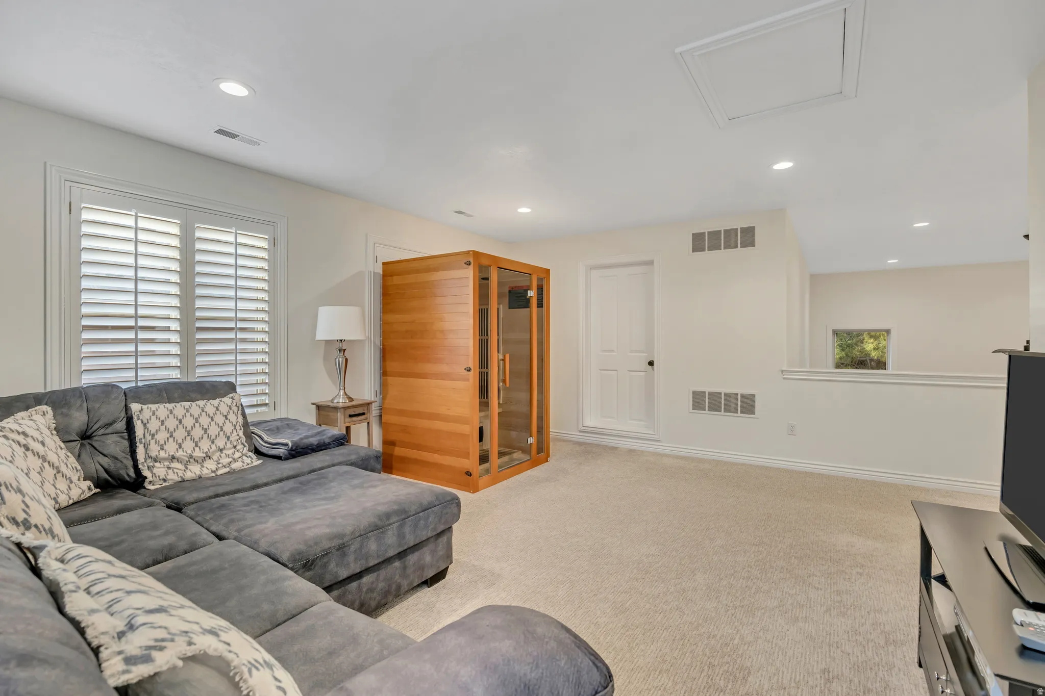 Carpeted entertainment area featuring a built-in sauna with glass panels, recessed lighting, and window with plantation shutters