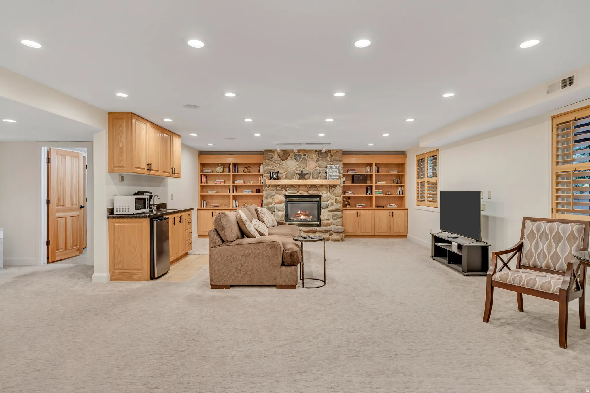 Spacious recreation room featuring recessed lighting, a stone-faced fireplace, and custom built-in cabinetry with shelving