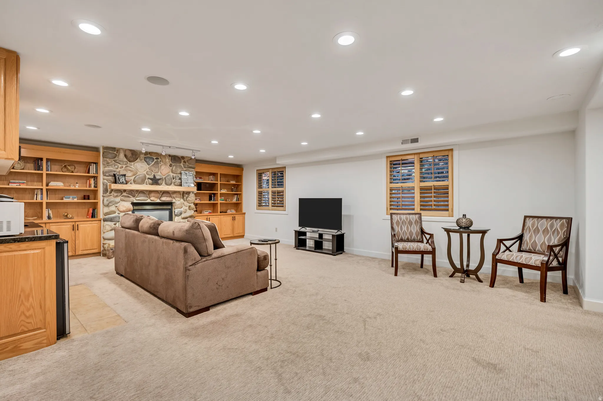 Spacious finished room featuring a stone-clad fireplace, extensive built-in shelving, recessed ceiling lighting, and light-colored carpeting