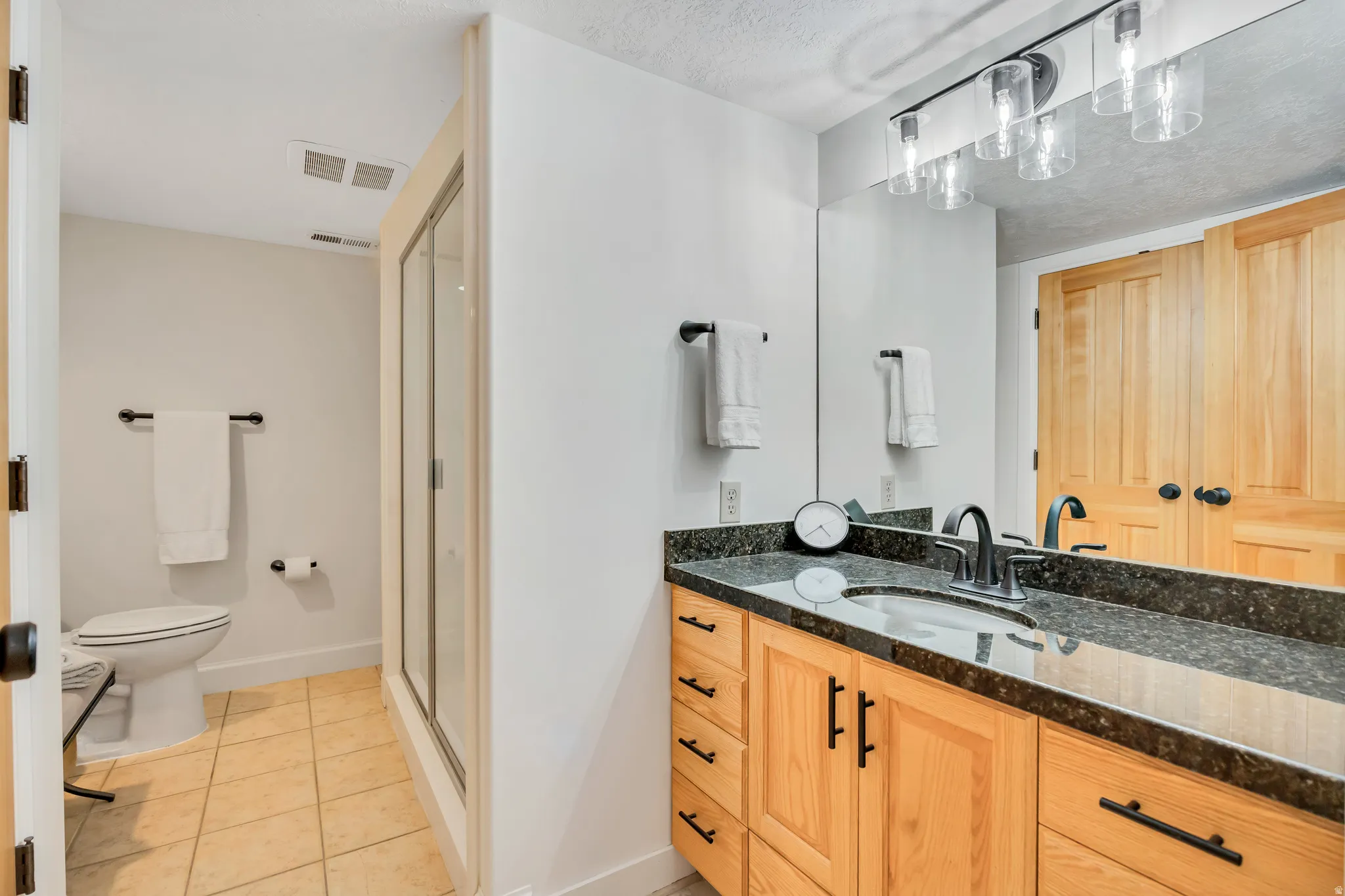 Bathroom with a natural wood vanity featuring a dark countertop and integrated sink