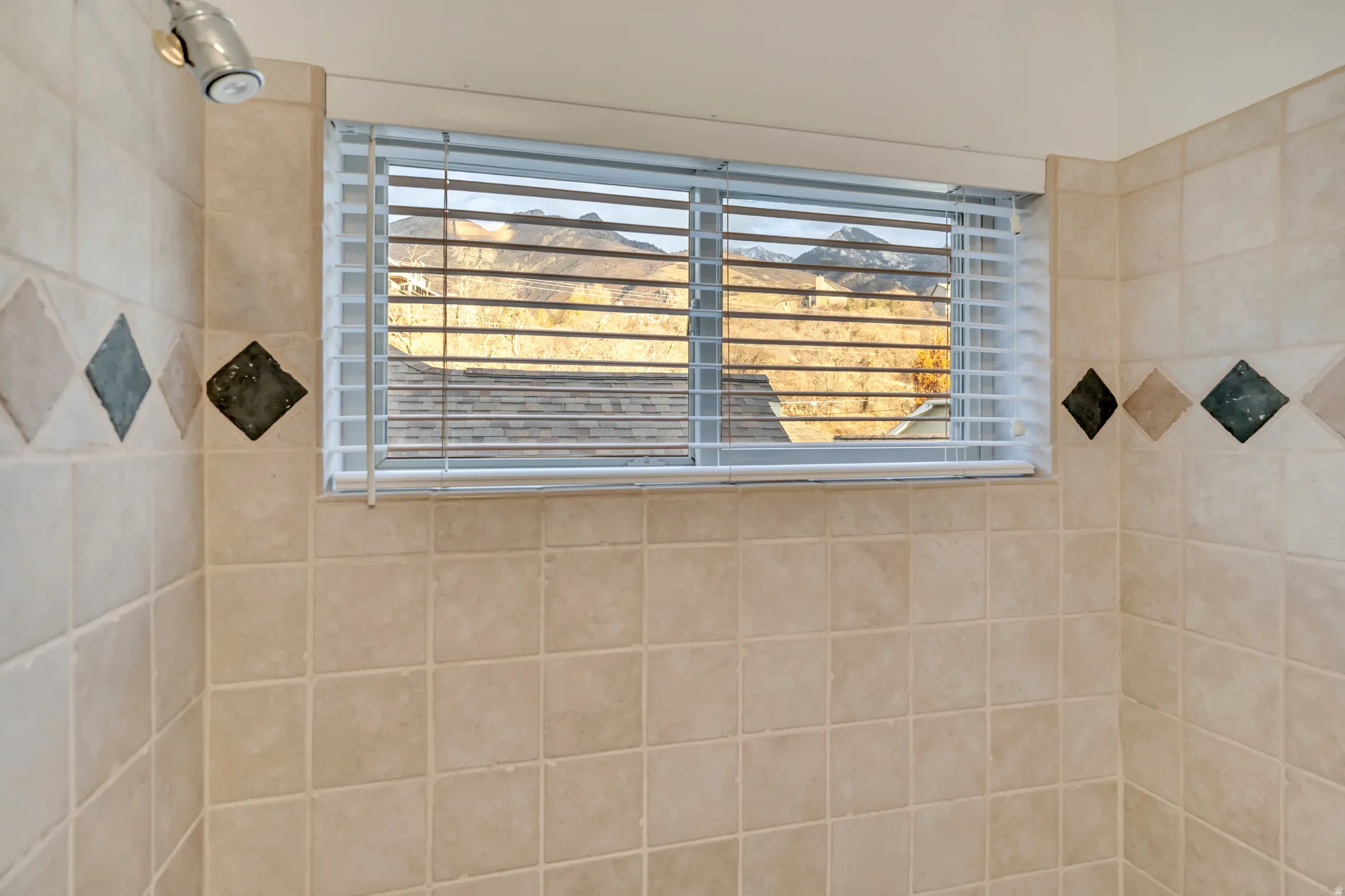 Shower enclosure with light-toned square wall tiles and a decorative diamond-patterned accent band