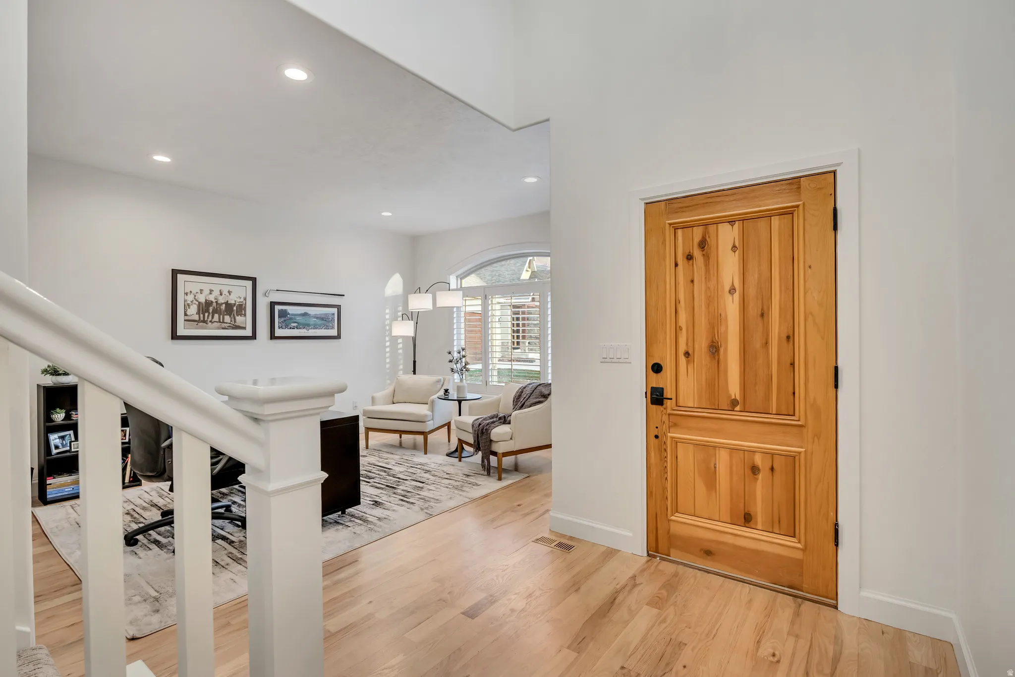 Solid wood panel door with dark hardware, light wood-finish flooring, white baseboards, and a white staircase with a prominent newel post