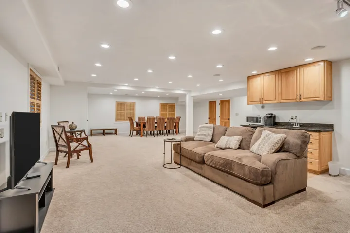 Carpeted recreation area featuring recessed lighting, a wet bar with wood cabinetry and dark countertops, and interior window shutters