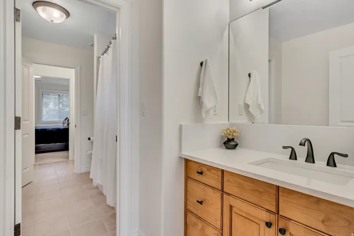 Bathroom vanity with light wood-finish cabinetry, a white countertop, and a built-in sink with a matte black faucet