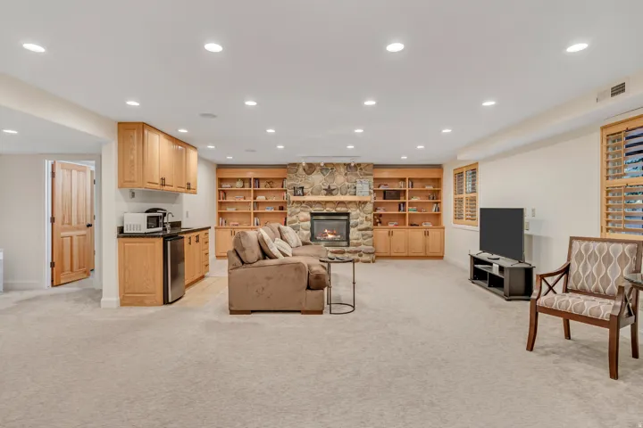 Spacious recreation room featuring recessed lighting, a stone-faced fireplace, and custom built-in cabinetry with shelving