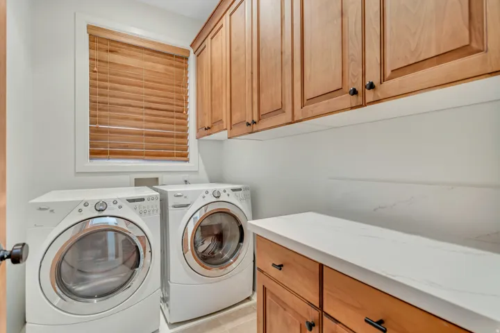Dedicated laundry room featuring light wood cabinetry, white countertops, a window with wood blinds, and light-colored flooring