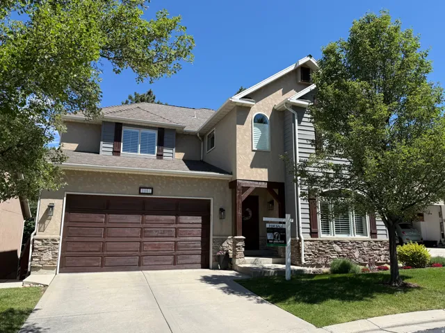 Two-story residence featuring a combination of stucco and siding exteriors, a stone veneer foundation, and a prominent dark wood-paneled garage door