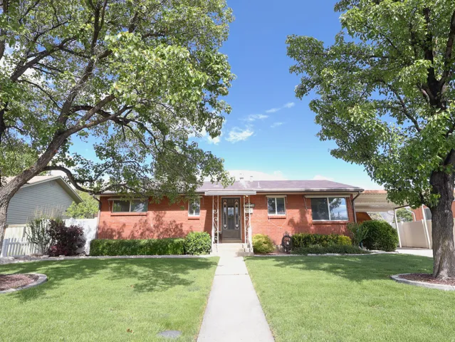 Brick exterior residence featuring a green lawn, established shade trees, a concrete walkway, and a carport