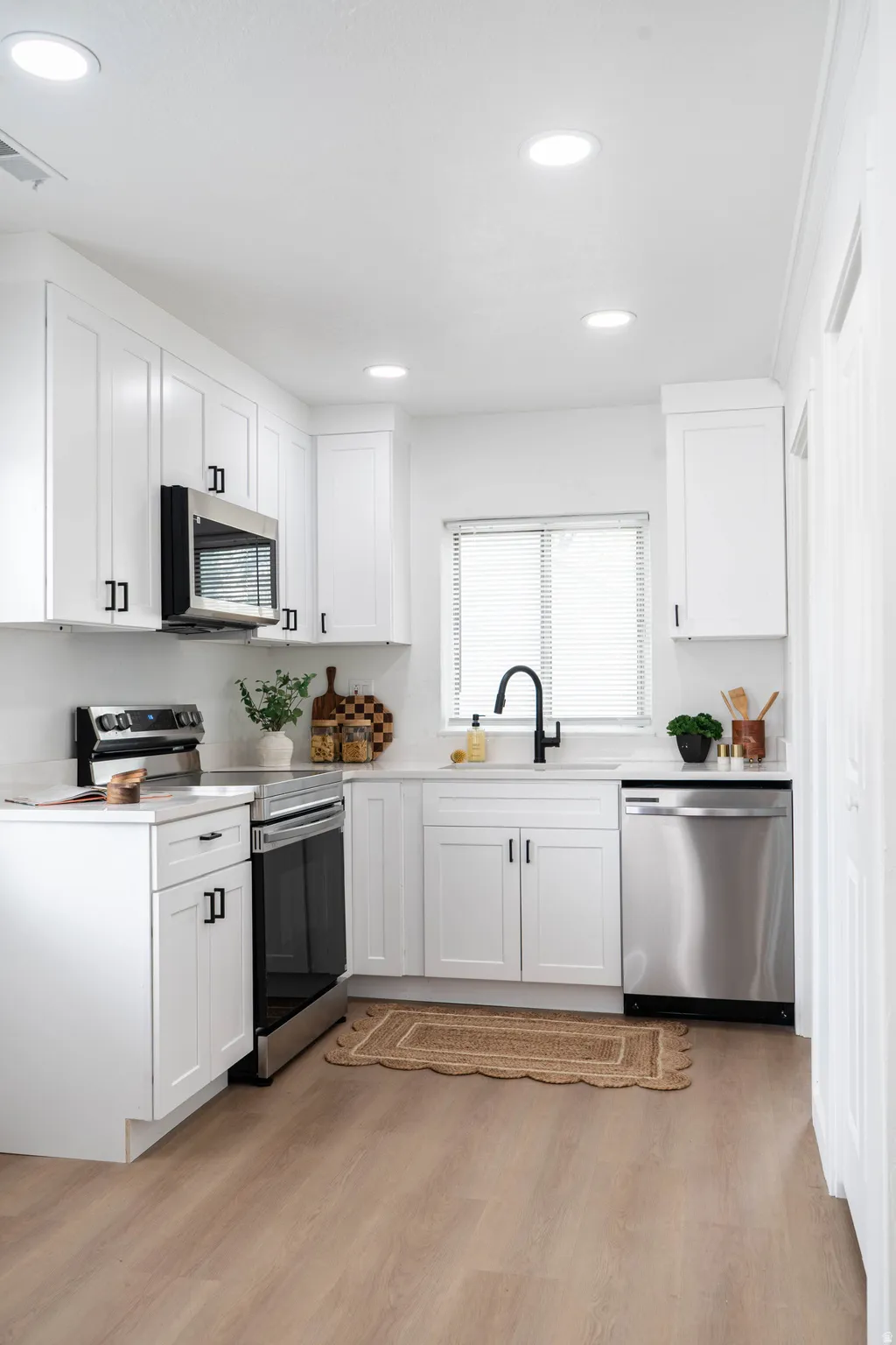 Contemporary kitchen featuring white cabinetry, stainless steel appliances, light-toned wood-finish flooring, recessed lighting, and a window with blinds