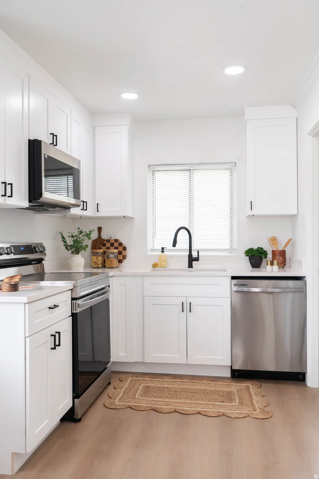 Bright kitchen featuring white shaker cabinetry, stainless steel appliances, a black gooseneck faucet, light countertops, and wood-finish flooring