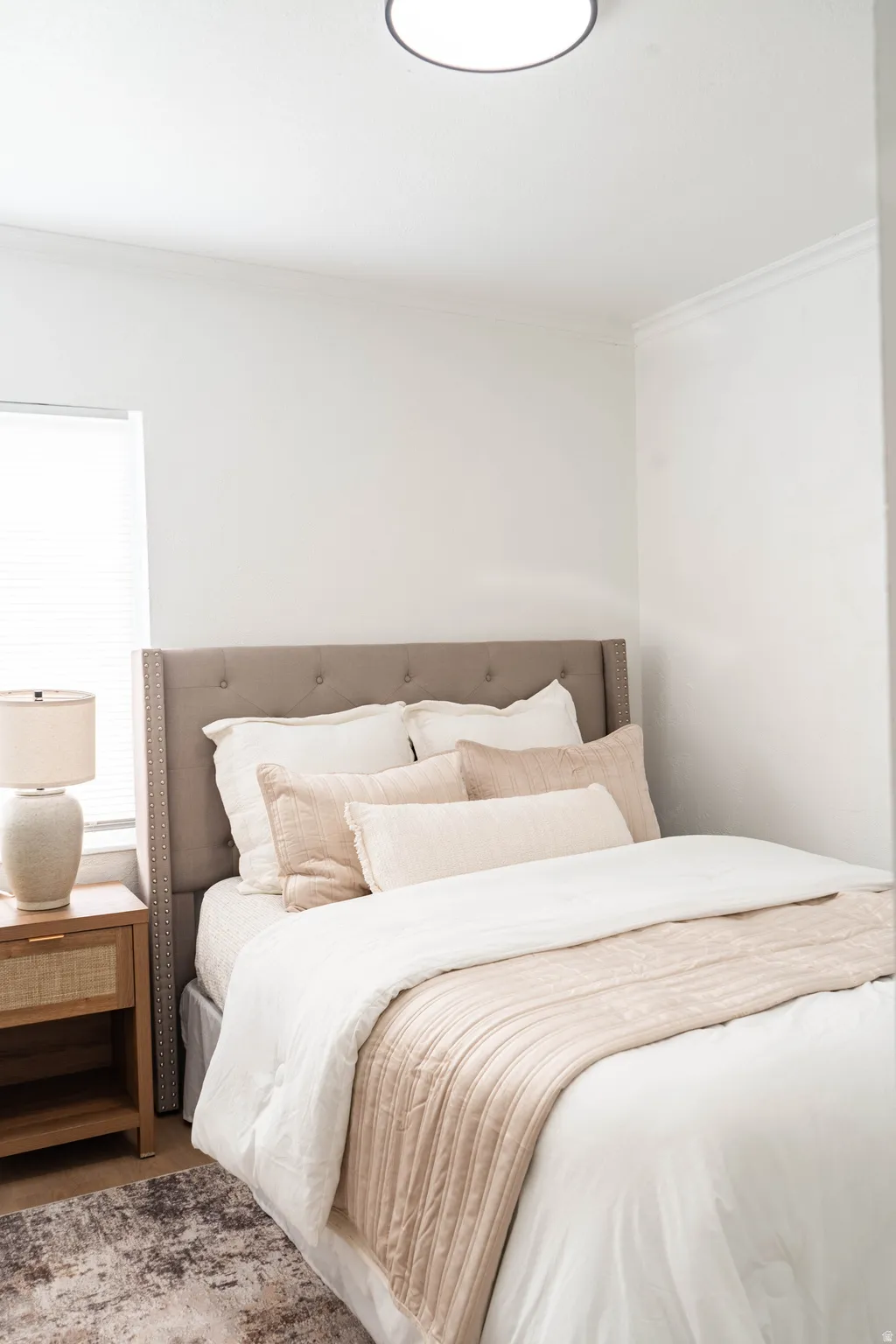 Light-filled bedroom featuring a neutral color palette, crown molding, and wood-finish flooring