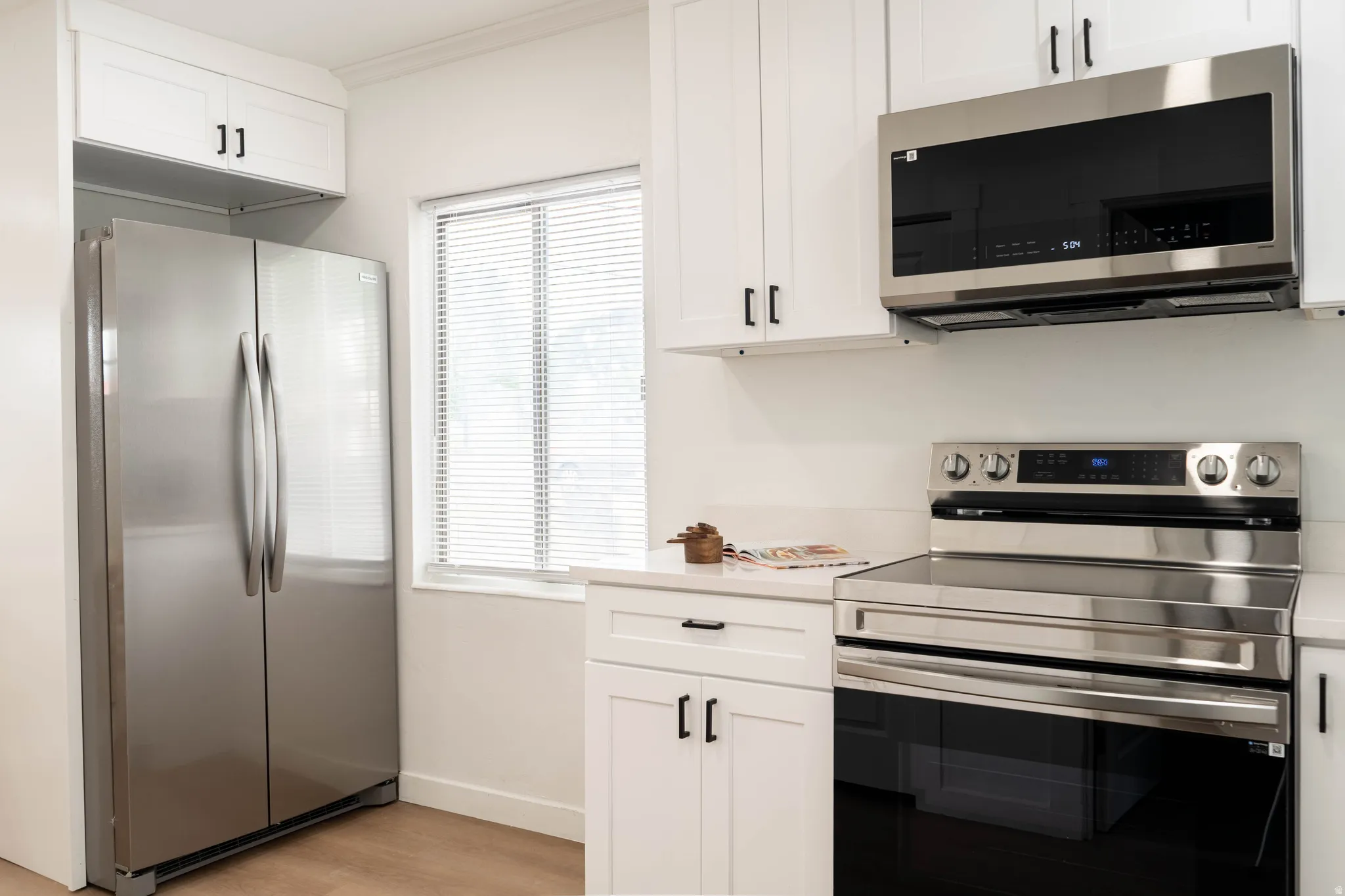 Kitchen showcasing white cabinetry, stainless steel appliances, a built-in microwave, and a window with blinds