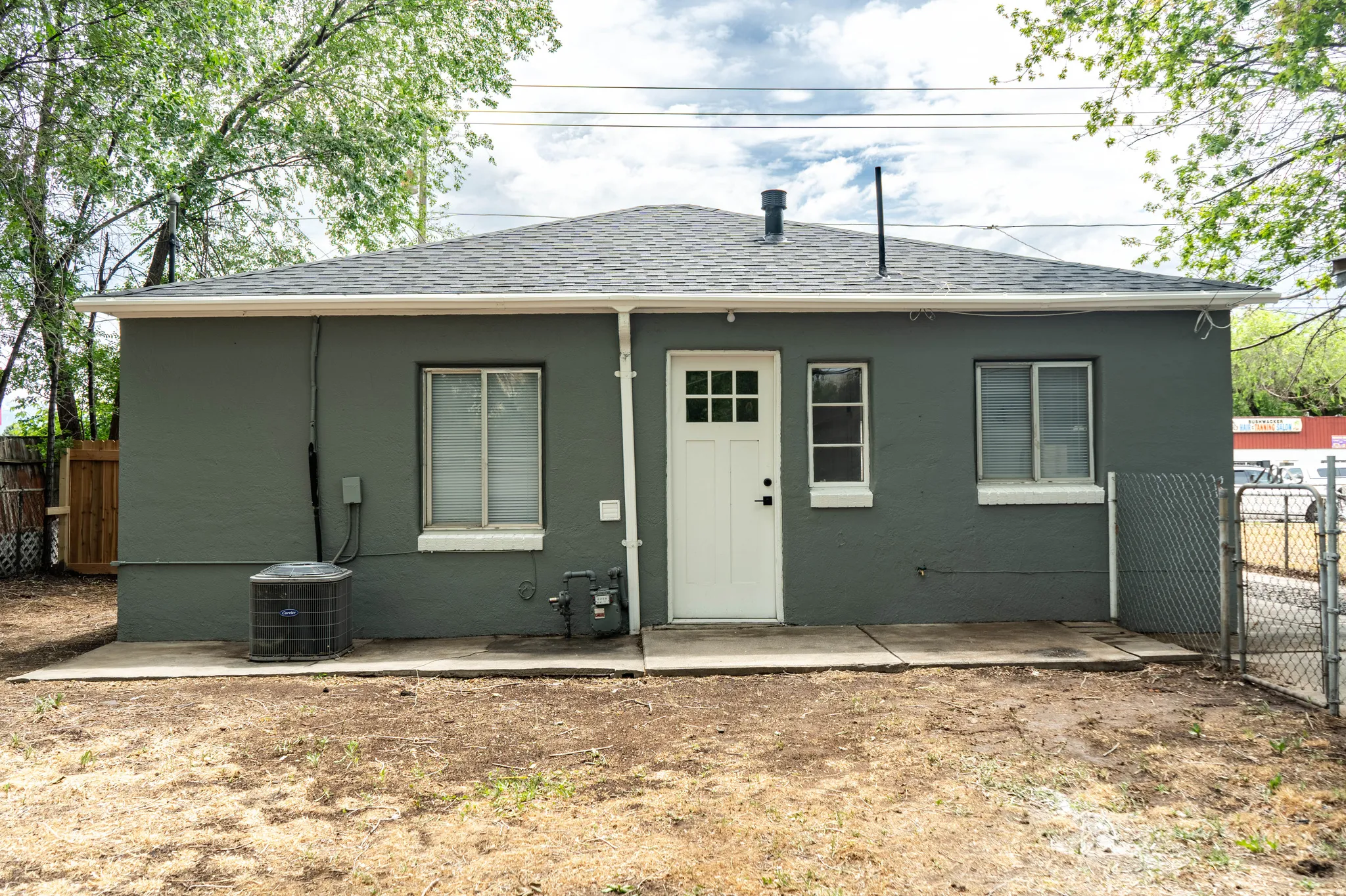 Rear exterior featuring a grey stucco finish, white paneled door with grid glass, and dark shingle roofing