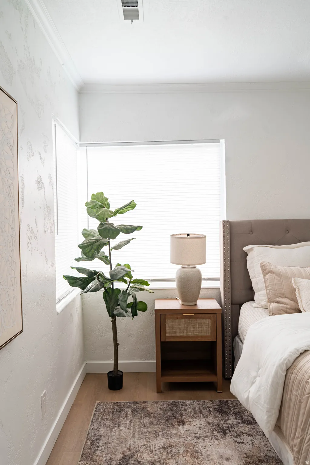 Corner bedroom area featuring wood-finish flooring, crown molding, and a large window with horizontal blinds