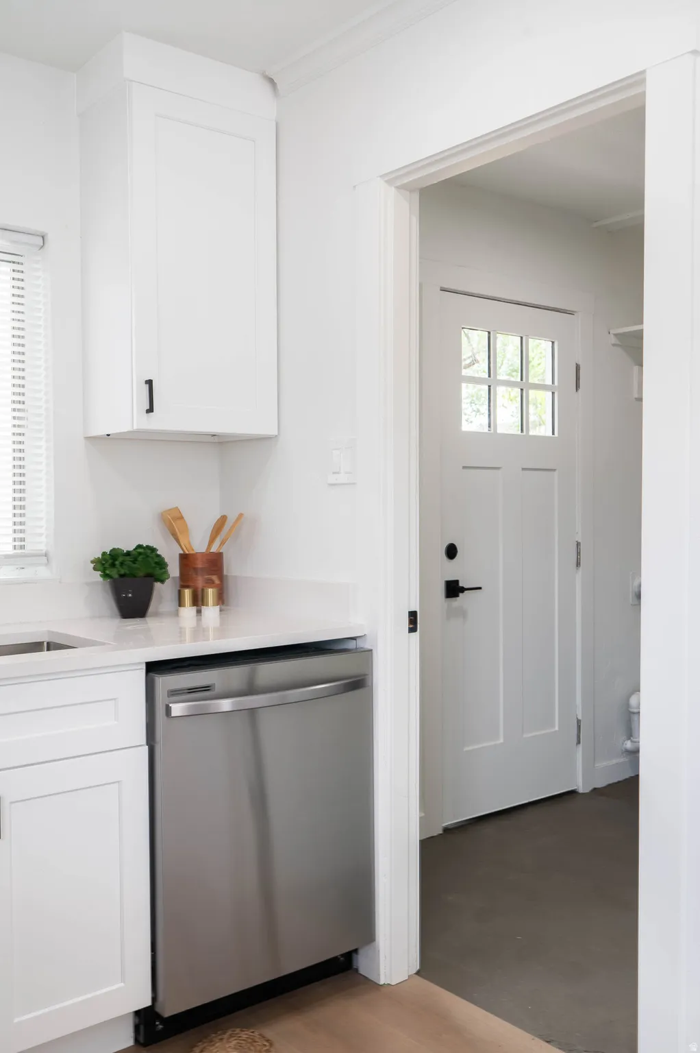 Modern kitchen area featuring white shaker cabinetry with black hardware, a stainless steel dishwasher, and light-toned countertops