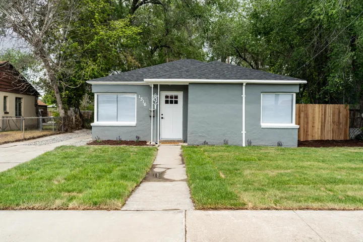 Contemporary bungalow featuring a gray stucco exterior, white trim, and a dark shingle roof