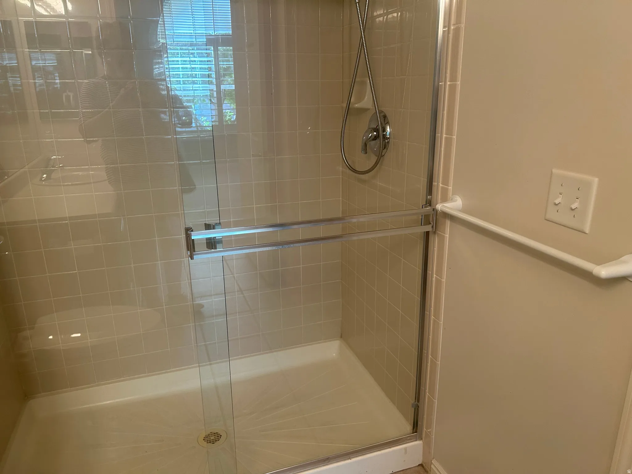 Enclosed shower with clear glass sliding doors, featuring beige square tiles and a white shower base