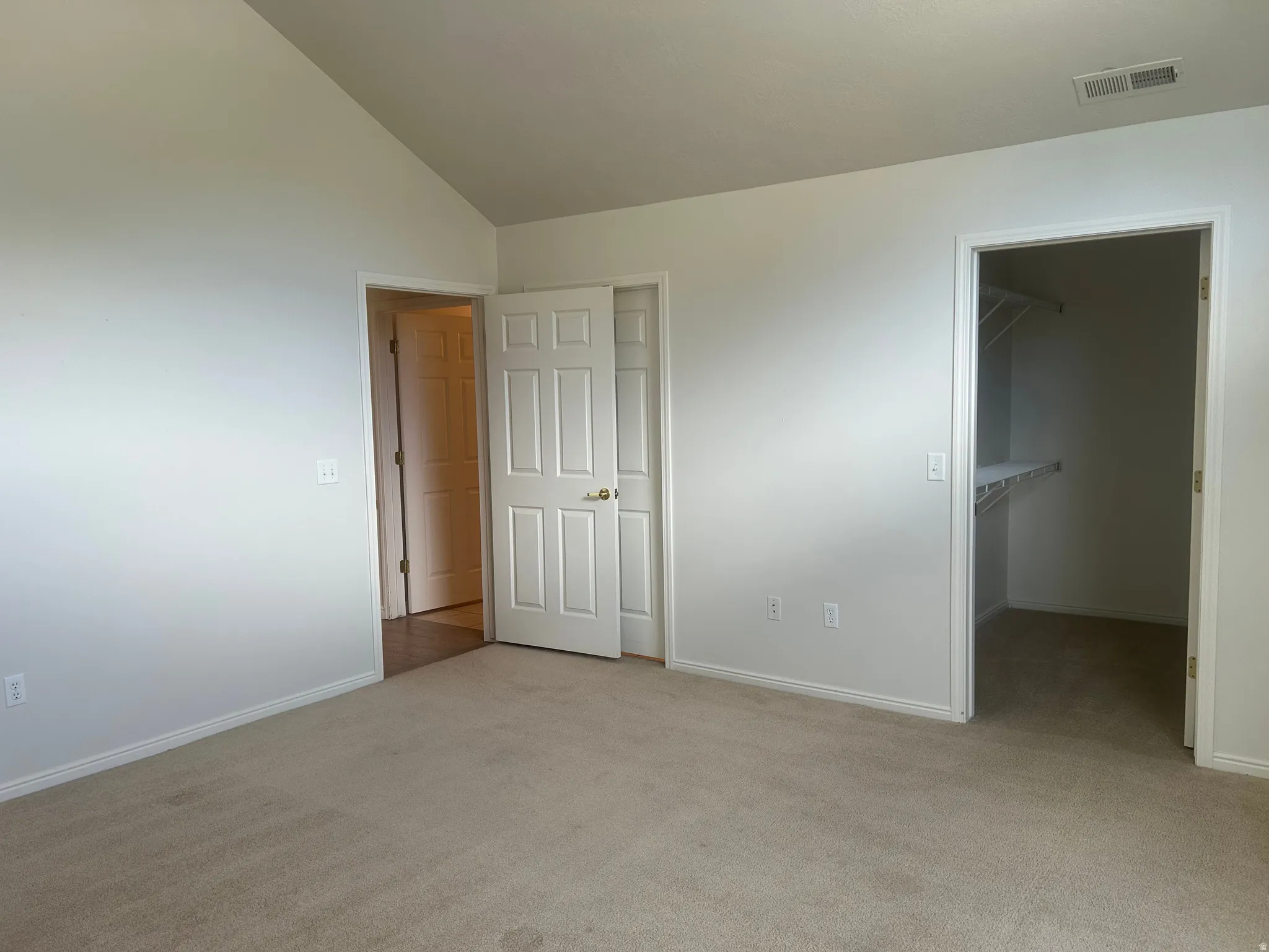 Spacious room featuring vaulted ceilings, light-toned carpeting, white trim, and a walk-in closet with built-in shelving